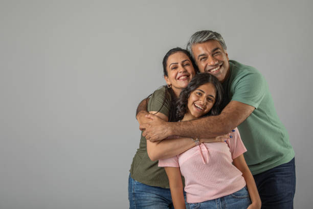 Portrait of happy loving Indian mother and father embracing daughter while standing against white background