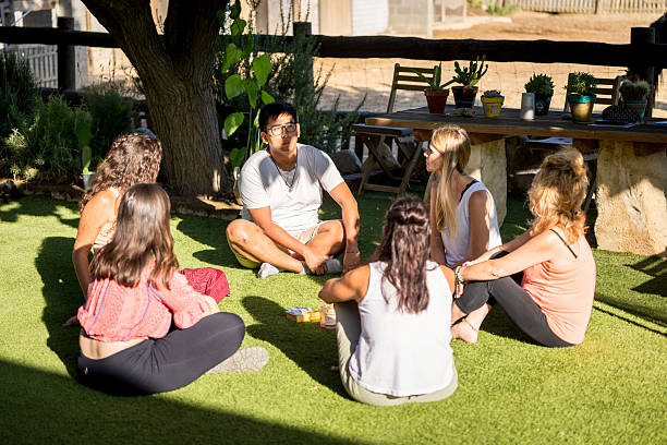 Group therapy session unfolding outdoors, participants seated in grassy circle, collaboratively processing personal experiences with professional counseling guidance