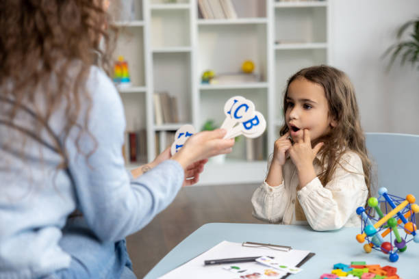 Speech practice. Speech therapist showing letters to a girl while having a training session