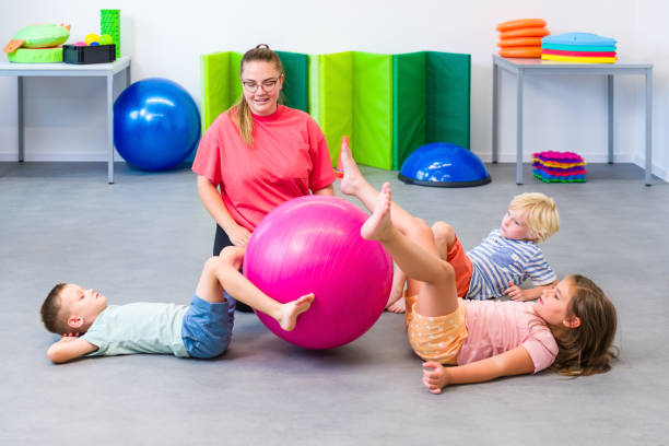 Kids group physical therapy. Children and female physical therapist exercising during session. Bilateral coordination or integration.