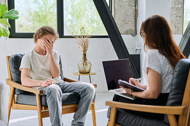 Sad unhappy teenage boy in mental therapy session, talking with behavioral specialist psychologist counselor, social worker. Adolescence mental health care support advice help psychology psychotherapy